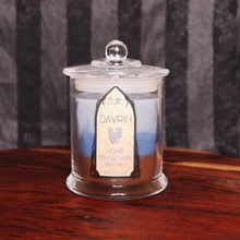 Load image into Gallery viewer, A grey candle labeled 'Davrin's Blend' with layers of blue and brown wax, sitting on a wooden surface.