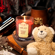 Load image into Gallery viewer, A lit red soy candle with swirls of black wax spreading through it. Label reads "Karlach, Woodsmoke, Cinnamon, Motor Oil. Baldur's Gate 3 Inspired Candle" There is a teddy bear named Clive in the foreground.