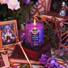 Load image into Gallery viewer, Purple candle labeled 'Meera Octavia -Plum Jasmine Cedar' on a wooden stand with a gold sword and decorative elements.
