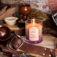 Load image into Gallery viewer, A tan and purple candle surrounded by leather, pottery and swords. Label reads "Minsc - Chocolate, Plums, Sandalwood - Baldur's Gate 3 Inspired Candle"