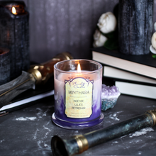 Load image into Gallery viewer, A white and purple candle surrounded by books, daggers and black candles. Label reads "Minthara - Incense, Lilies, Petrichor - Baldur's Gate 3 Inspired Candle"