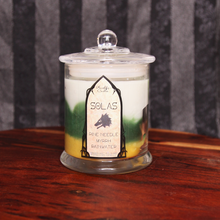Load image into Gallery viewer, A soy candle labeled 'Solas's Blend' with layers of white, green and gold wax, sitting on a wooden surface.