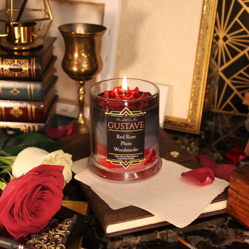 A red, black and grey candle with a red wax rose sits surrounded by red and white rose petals, canvases and art deco inspired decor.
The label reads 