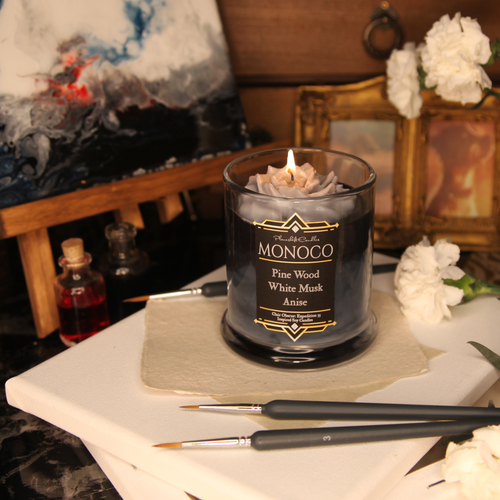A lit grey wax rose sits on black, grey and white tinted candle. The label reads 