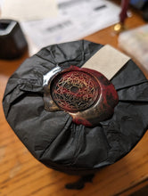 Load image into Gallery viewer, A red and black wax seal stamped on top of a packaged custom candle.
